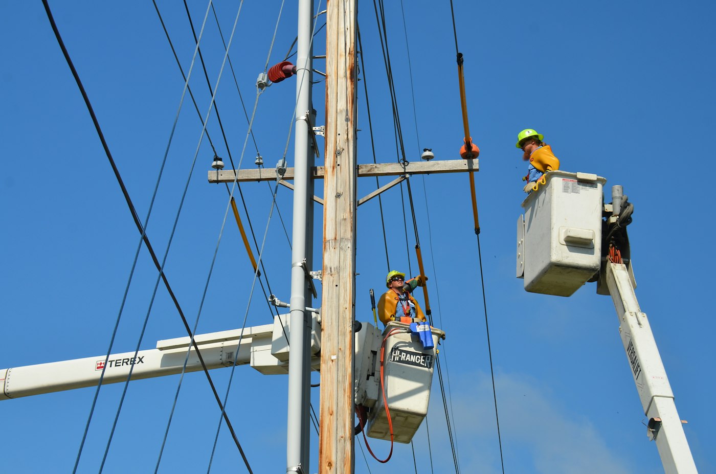 Two line workers on power lines from bucket trucks